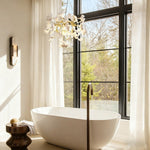 Gold-tone ceramic leaf round chandelier beside a bathroom window.