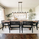 Black cylinder linear chandelier above a wooden dining table and dark chairs.
