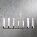 Seven clear glass cylinders on a black linear chandelier.