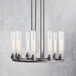 Black ring chandelier with upright clear glass cylinders against a gray wall.
