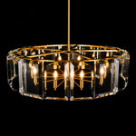 Illuminated brass-tone crystal-bar drum chandelier against a dark background.