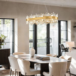 Gold-tone crystal ribbon oval chandelier above a dining table beside glass doors.