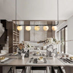 Alabaster globe linear chandelier above a set dining table, seen from the front.