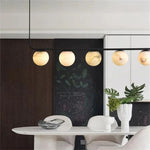 Black linear chandelier with alabaster globes above a white table.