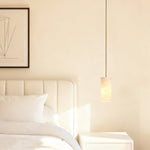 Gold-tone cylindrical alabaster pendant beside a bed.