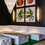 A pair of illuminated selenite sconces flanking artwork above a curved sofa.