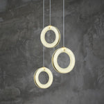 Three illuminated alabaster rings hanging at staggered heights against a gray wall.