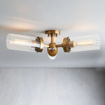 Brass-tone flush mount with three horizontal clear glass cylinders on a ceiling.