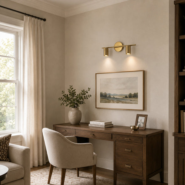 Brass twin-cylinder picture light illuminating framed artwork above a home office desk