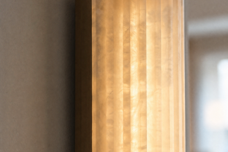 Illuminated alabaster wall sconce showing softly veined stone and a warm metal backplate