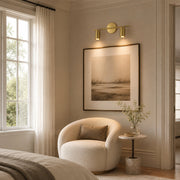 Twin-head brass picture light illuminating framed artwork in a warm bedroom sitting area