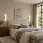 Two brass-tone cylindrical sconces beside a bed and framed artwork.
