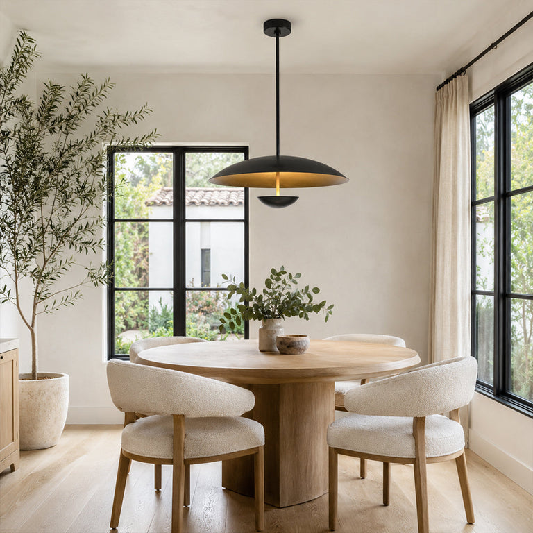 Black disc pendant above a round dining table beside tall windows