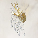 Brass branch wall sconce with clear crystal pendants on a warm textured wall