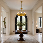 Candle ring chandelier above a dark round table in an arched entrance hall.