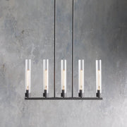 Five clear glass cylinders on a black linear chandelier against a gray wall.