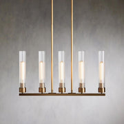 Five clear glass cylinders on a brass-tone linear chandelier against a gray wall.