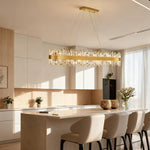 Gold-tone crystal ribbon oval chandelier above a sunlit kitchen island.