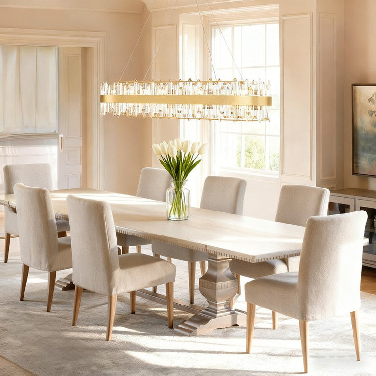 Gold-tone crystal ribbon oval chandelier above a white dining table.