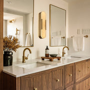 Brass alabaster pill wall sconce illuminated between bathroom mirrors