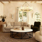Gold-tone ring chandelier above a round coffee table beside a dark armchair.