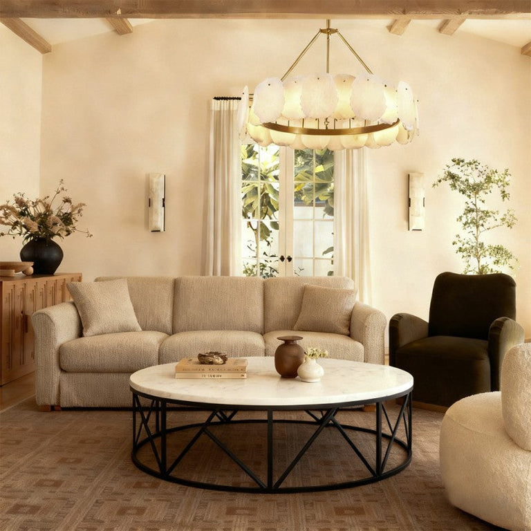 Gold-tone ring chandelier above a round coffee table beside a dark armchair.