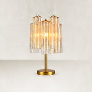 Glass tube table lamp with a gold-tone stem and round base, illuminated on a plain background.