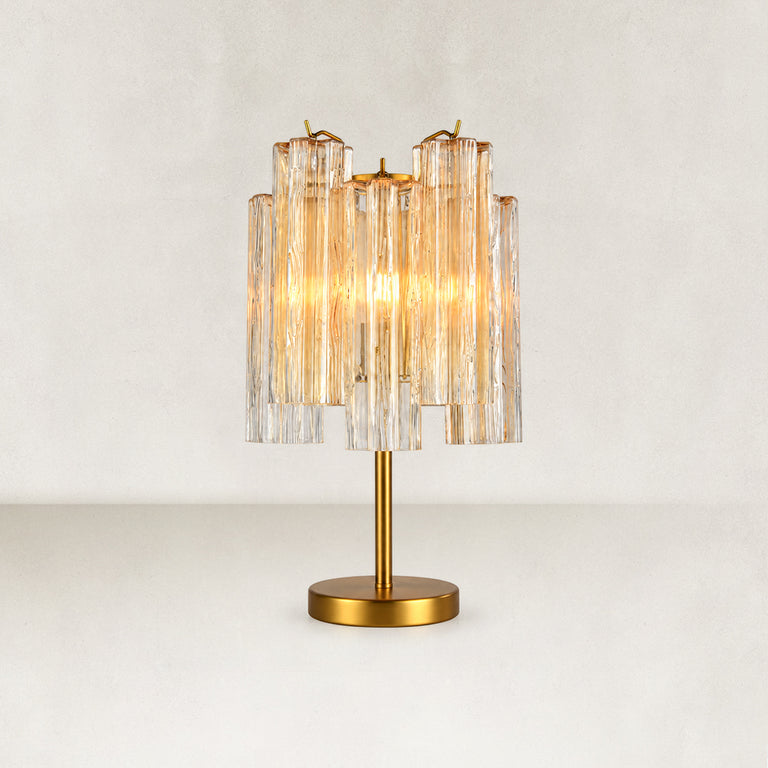 Glass tube table lamp with a gold-tone stem and round base, illuminated on a plain background.