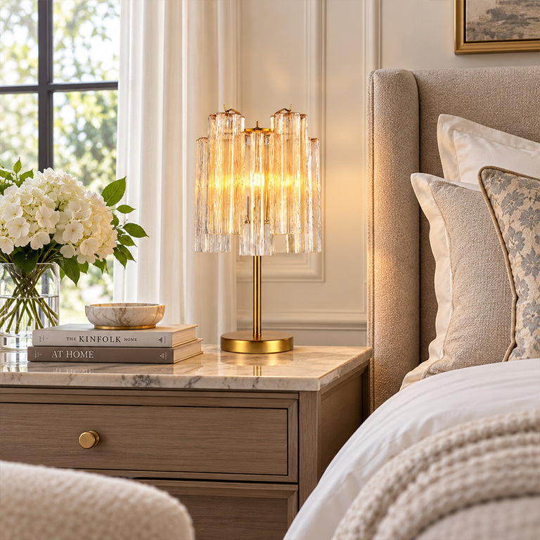 Glass tube table lamp with a gold-tone base on a bedside table.