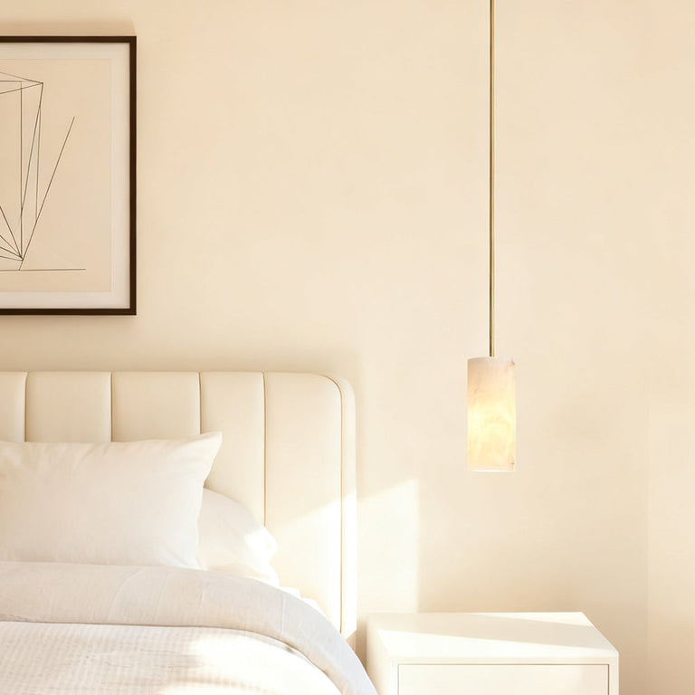 Gold-tone cylindrical alabaster pendant beside a bed.