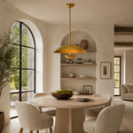 Gold-tone disc pendant above a round dining table by arched shelving