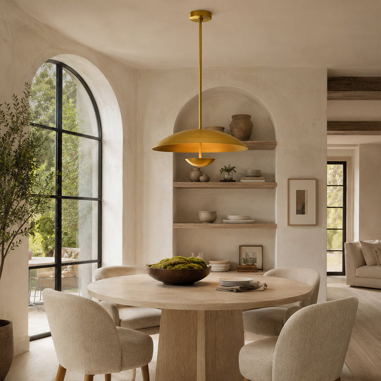 Gold-tone disc pendant above a round dining table by arched shelving