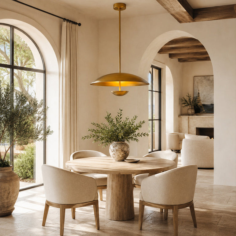 Gold-tone disc pendant above a round dining table near an arched window