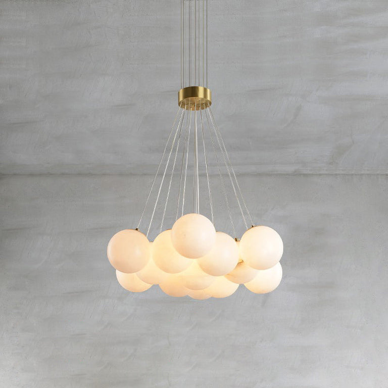 Illuminated alabaster globe cluster chandelier with brass-colored fittings against a gray wall