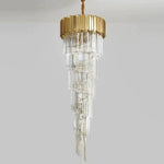 Long tapering crystal chandelier beneath a gold-tone crown against a neutral background.