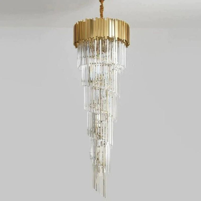 Long tapering crystal chandelier beneath a gold-tone crown against a neutral background.