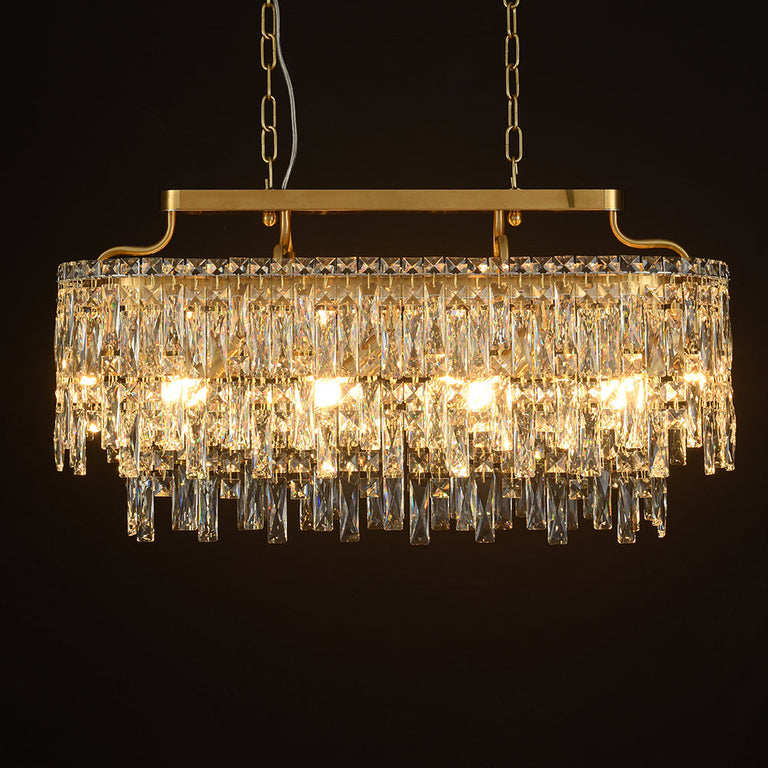 Gold-tone oval crystal chandelier, lit fixture against dark background.