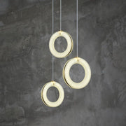 Three illuminated alabaster rings hanging at staggered heights against a gray wall.
