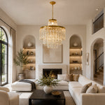Gold-tone tiered crystal drum chandelier beside a staircase and tall arched windows.