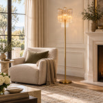 Gold-tone glass tube floor lamp beside an armchair near a fireplace.